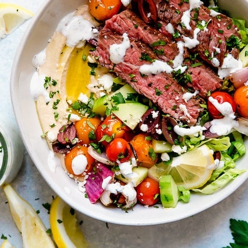 Birdseye view of Mediterranean Steak Bowls with hummus and drizzled with herb-yogurt dressing.