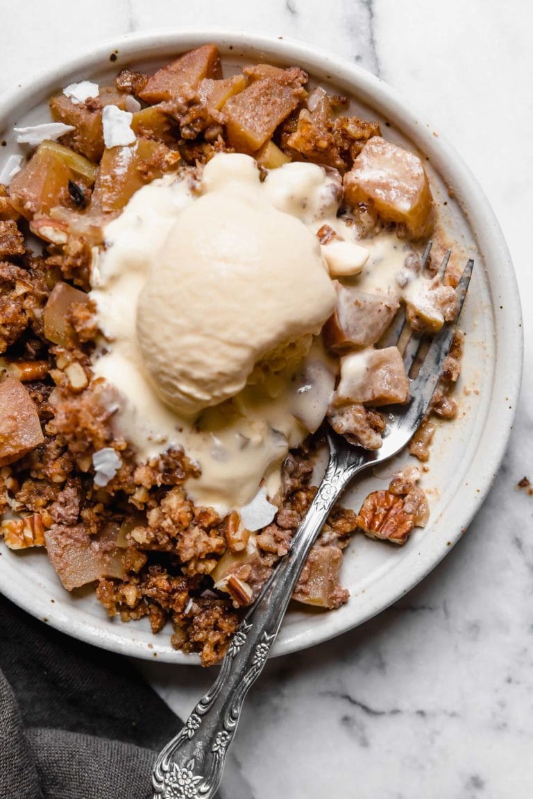 Close up view of a plate of freshly baked Paleo Apple Crisp topped with vanilla ice cream.