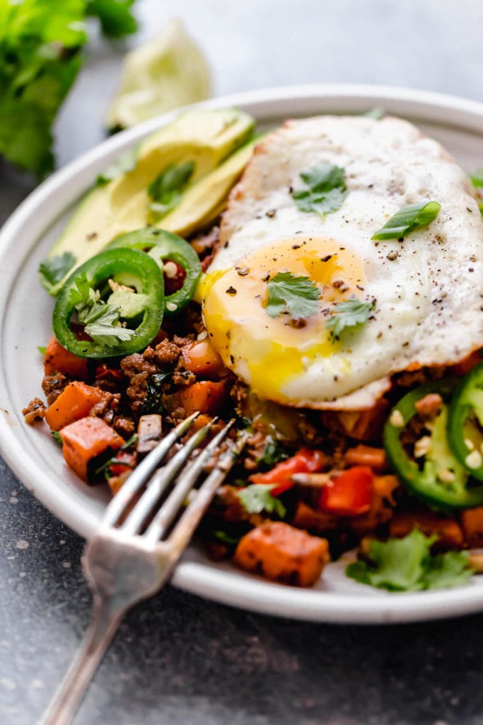 Tex-Mex Sweet Potato Hash served on a white plate with a fried-egg on top with the yolk running out of the egg.