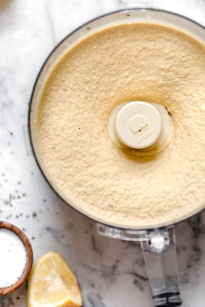 Overhead view food processor bowl filled with creamy and smooth garlic hummus