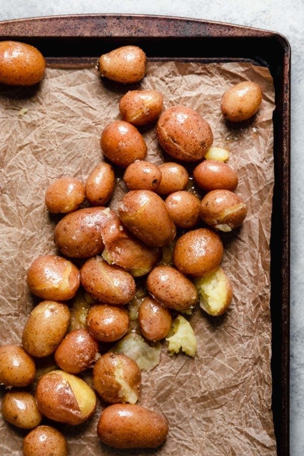 Softened potatoes on a parchment-covered baking sheet ready to be smashed.