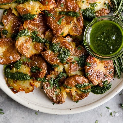 A plate full of crispy smashed potatoes drizzled with green garlic-herb oil.