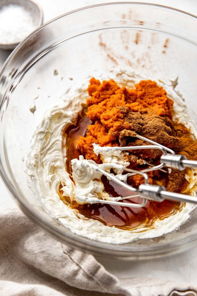 Close up view of a glass mixing bowl filled with Pumpkin Brownies ingredients being mixed with a hand mixer.