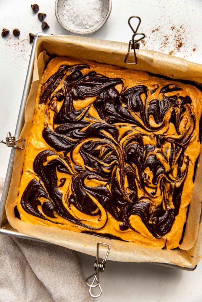 Overhead view of a pan of Pumpkin Brownie batter with swirls of different layers, ready for baking. 