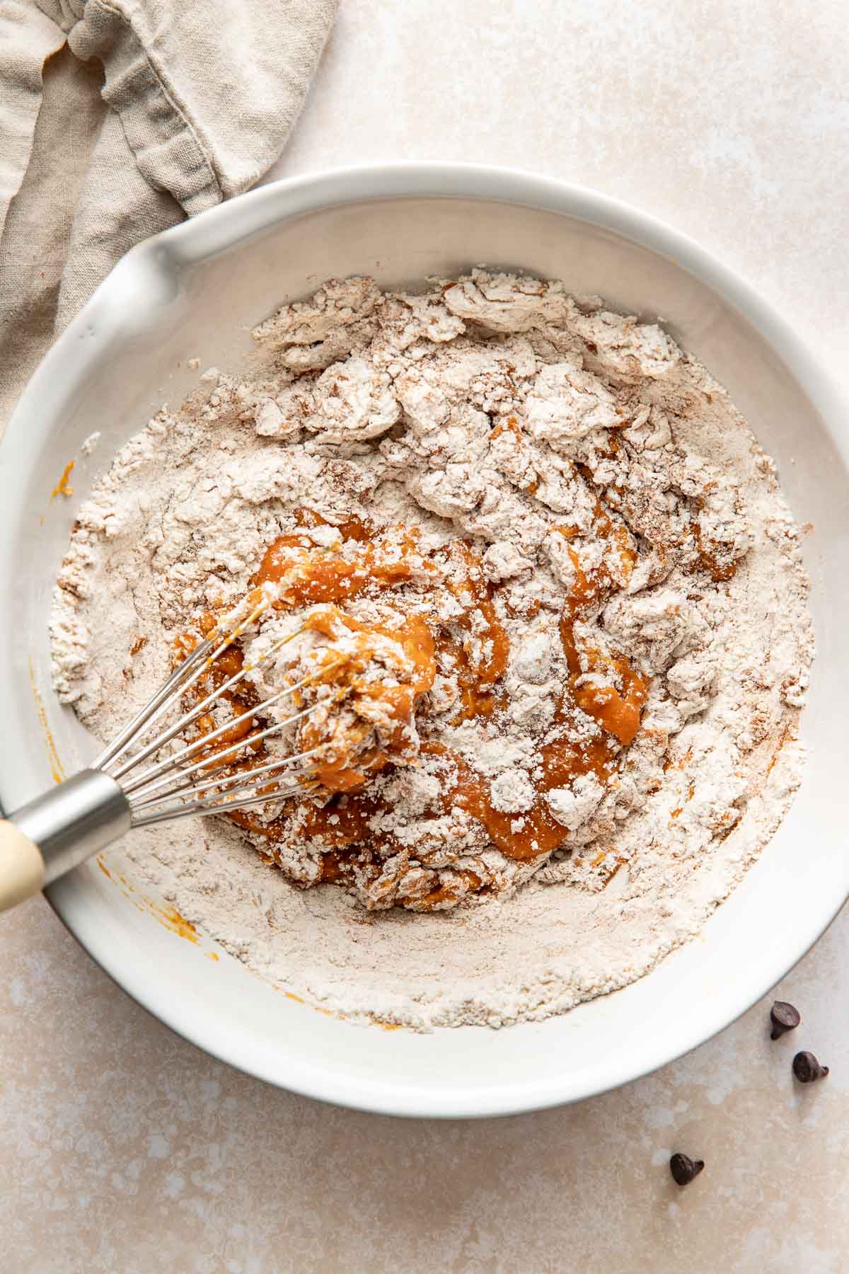 A hand using a whisk to mix pumpkin chocolate chip bar ingredients in a bowl.