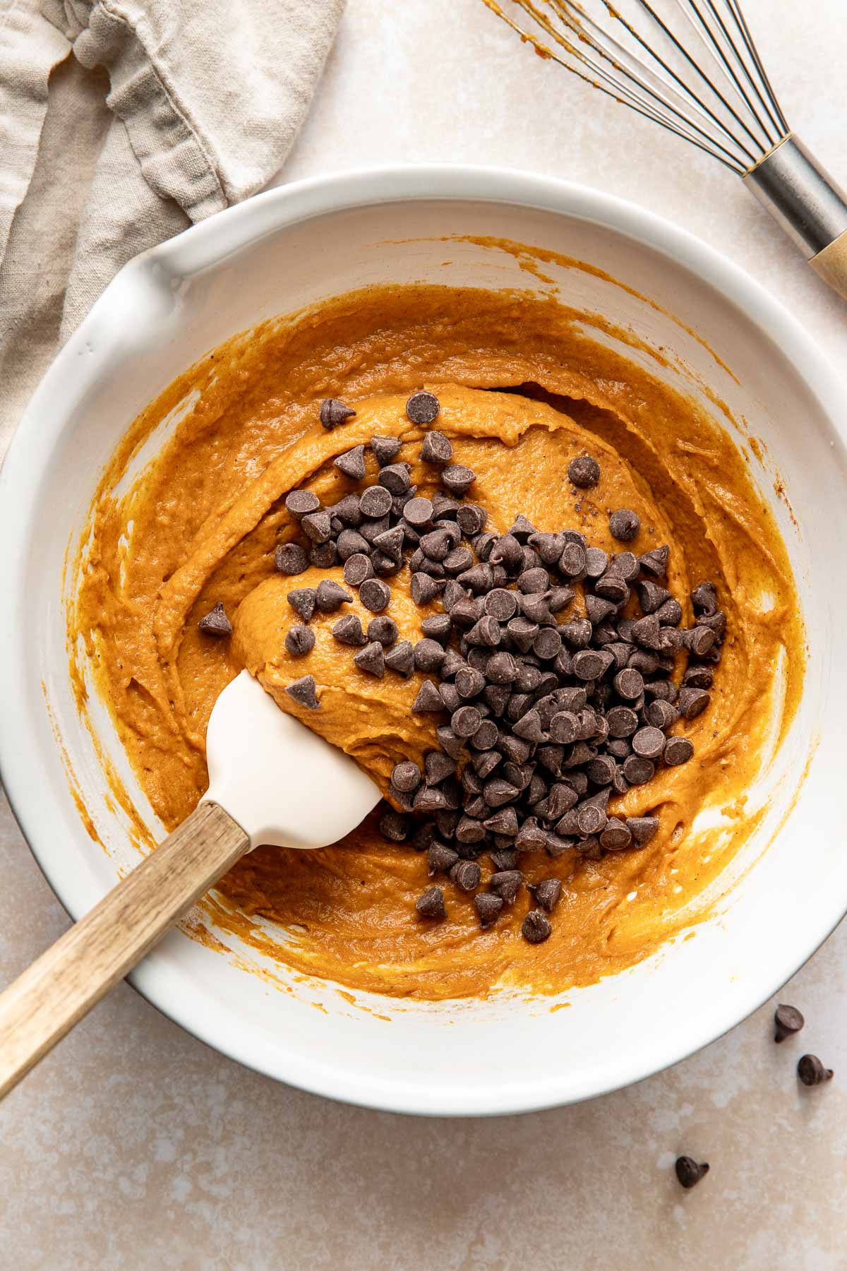 Chocolate chips being folded into pumpkin bar batter in a bowl.