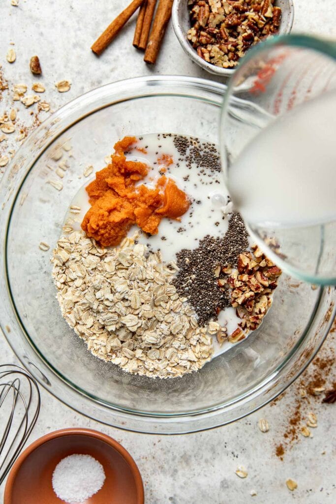 Overhead view of a glass bowl filled with ingredients for Pumpkin Overnight Oats ready to be stirred. 