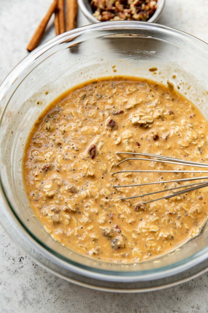 Overhead view of a glass bowl of freshly stirred ingredients for Pumpkin Overnight Oats. 