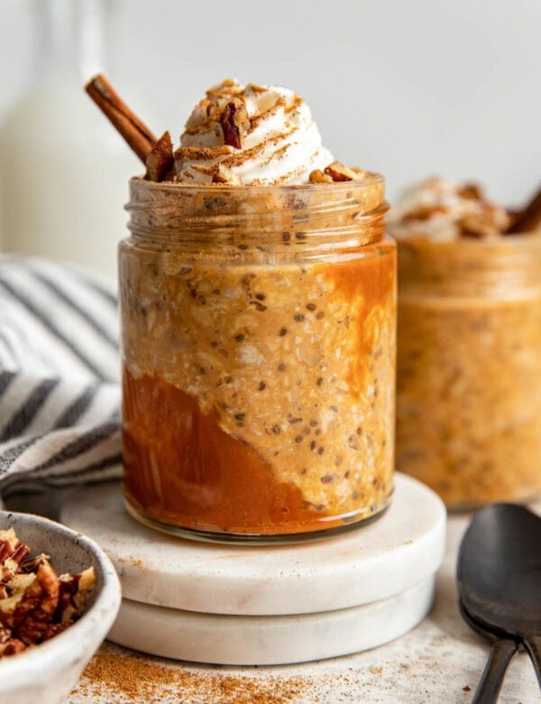 Side view jar filled with pumpkin overnight oats, topped with whipped cream and cinnamon stick