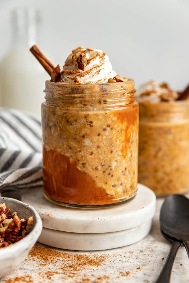 Side view jar filled with pumpkin overnight oats, topped with whipped cream and cinnamon stick