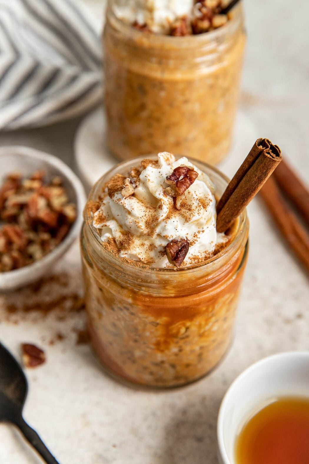 Overhead view of a jar of Pumpkin Overnight Oats topped with whipped cream, pecan pieces, and a cinnamon stick. 