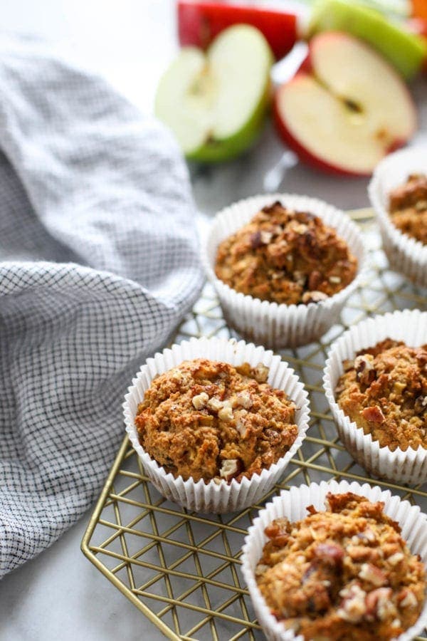 Paleo Morning Glory Muffins on a gold wire cooling rack with apples in the background. 