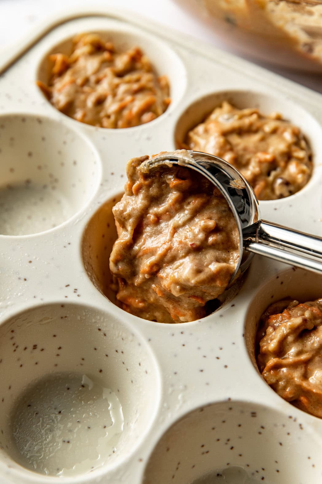 Close up view of a muffin pan being filled with Morning Glory Muffins dough. 