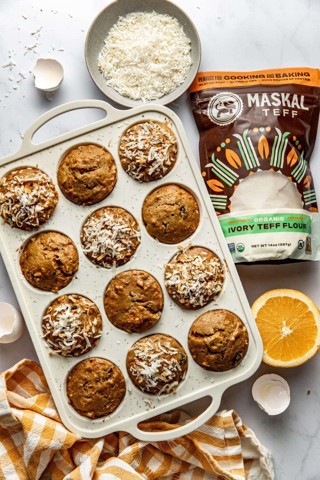 Overhead view of a pan of freshly baked Morning Glory Muffins next to a bag of Teff Flour. 