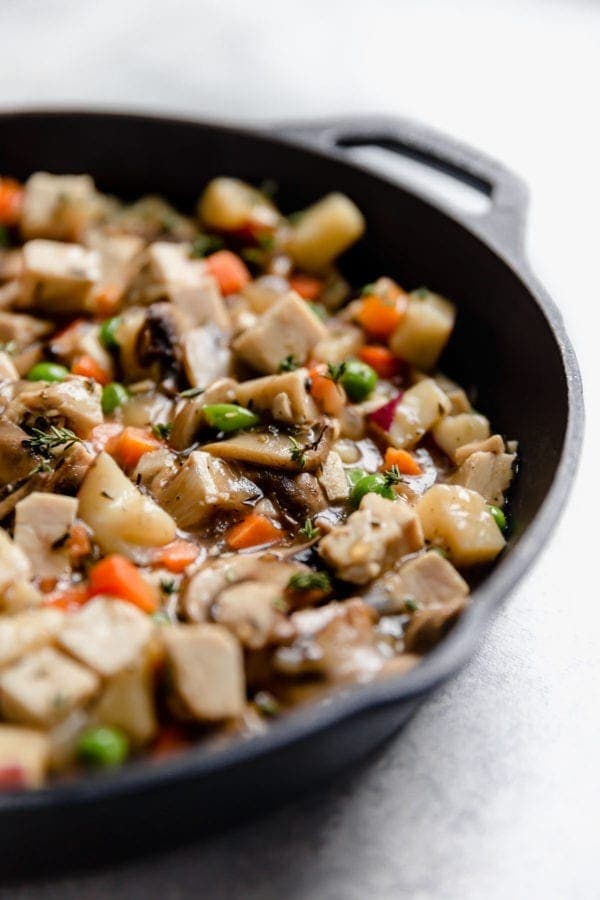 A black cast iron skillet is filled with the turkey and vegetable filling that will become a Paleo Turkey Pot Pie. 