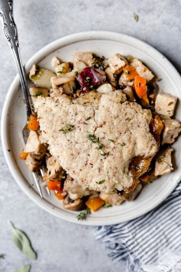A overhead view of a plate of turkey and vegetables in a thyme-sage gravy is topped with a flaky grain-free pastry crust in this Paleo Turkey Pot Pie. 
