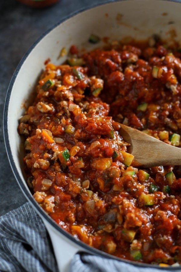 A white skillet filled with ground turkey, peppers, onions, zucchini and mixed with marinara sauce to create the filling for Pizza-Stuffed Spaghetti Squash.