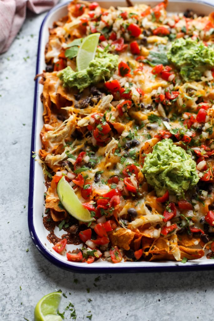 Close up view of Loaded Sweet Potato Nachos in a baking dish topped with melted shredded cheddar cheese and guacamole dollops.