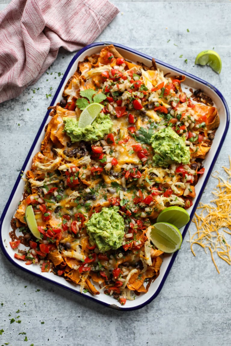 Overhead view baking sheet with loaded sweet potato nachos topped with melted cheese and guacamole
