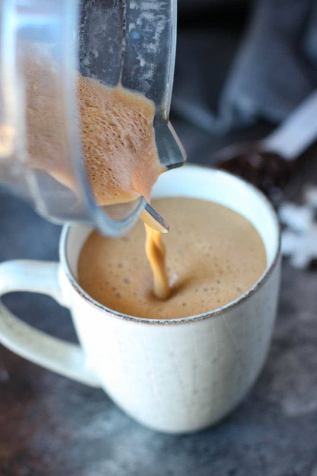 Cinnamon coconut latte being poured out of a blender into a coffee cup. 