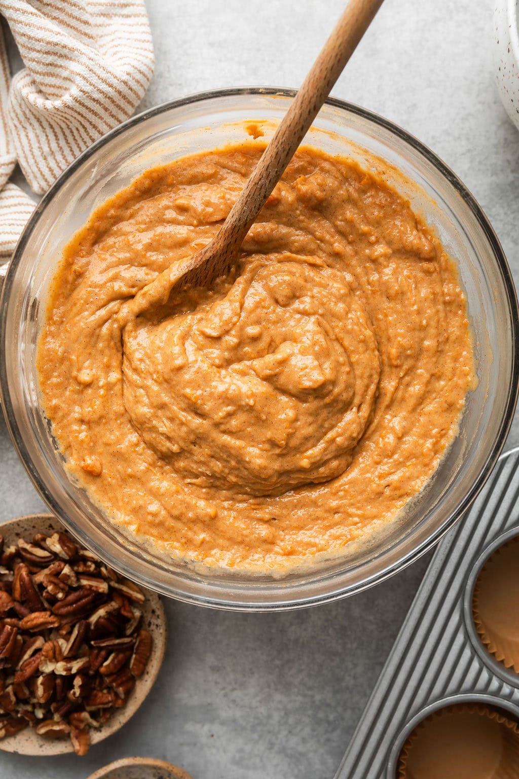 Overhead view of a glass bowl of mixed Sweet Potato Muffin batter with a wooden spoon in the batter.