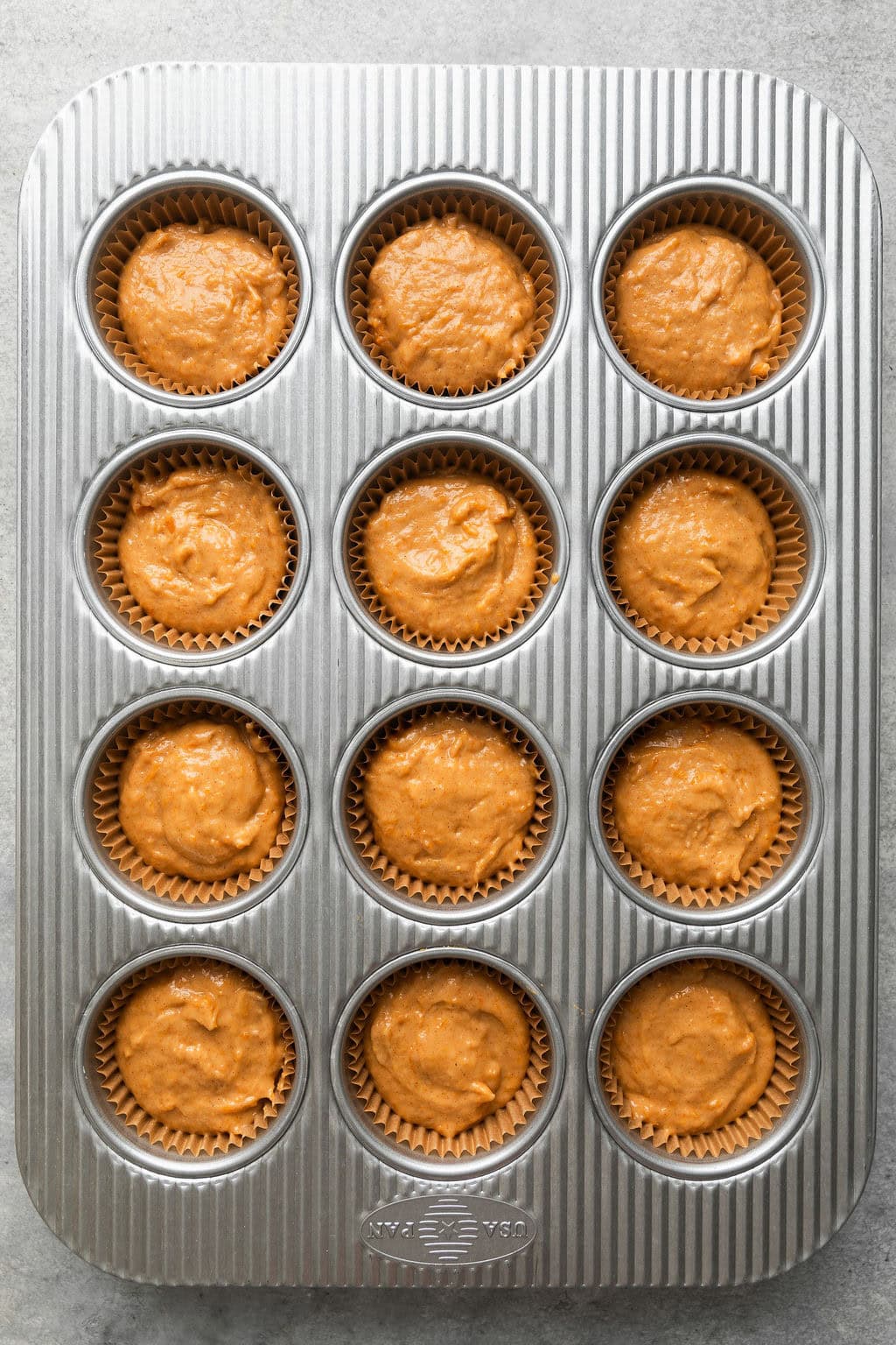 Overhead view of a metal muffin pan filled with Sweet Potato Muffin batter in each well ready for baking.