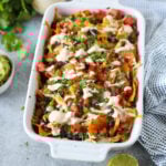 White ceramic casserole dish filled with sweet potato chips topped with melted cheese, shredded chicken, black beans, salsa, diced tomatoes, and a Southwest Ranch Dressing to create the ultimate Loaded Sweet Potato Nachos.