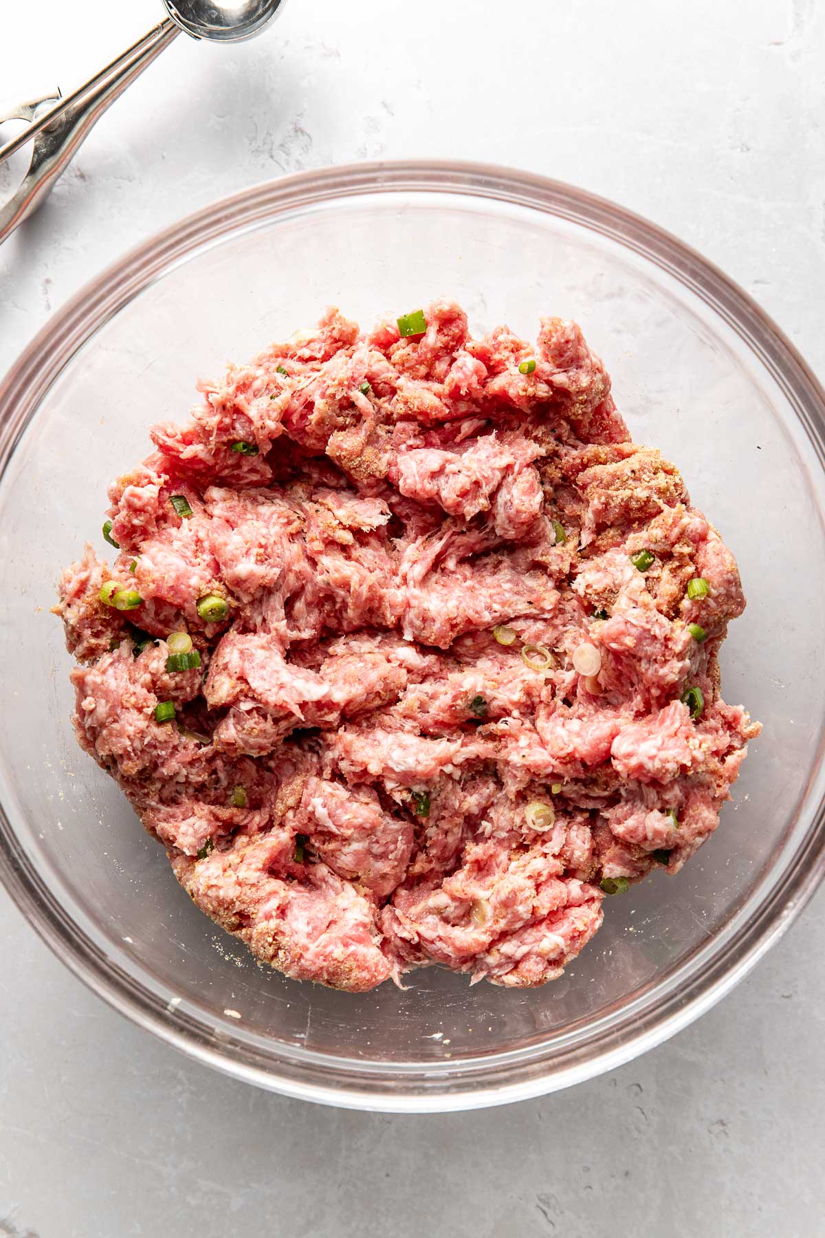 Overhead view of a glass bowl filled with ground pork and spices mixed together.