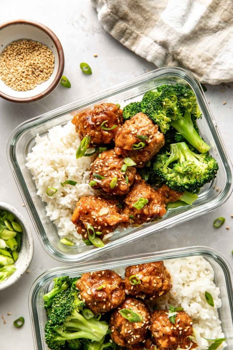 Overhead view of two glass meal prep containers filled with sweet and sour meatballswhite riceand broccoli topped with sesame seeds and green onions.