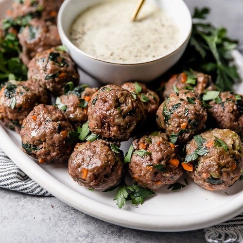 A white platter of the ultimate meal prep meatballs served with a small bowl of ranch dressing.