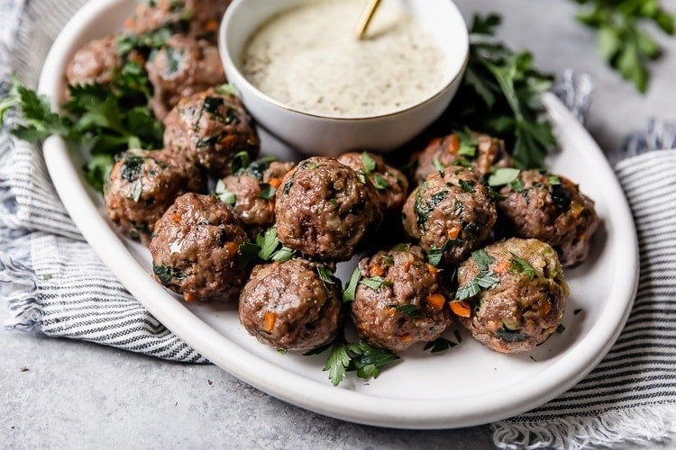 A white platter of the ultimate meal prep meatballs served with a small bowl of ranch dressing.