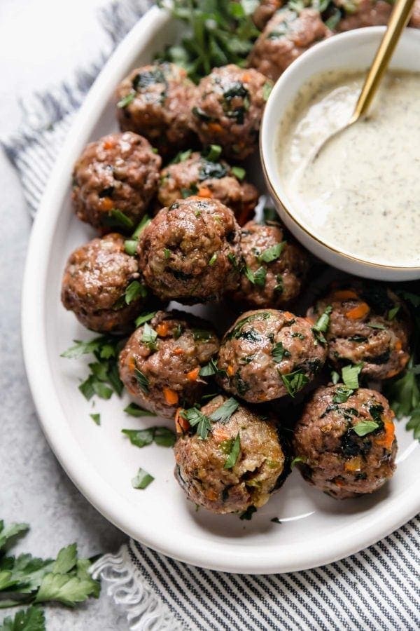 A white platter of the ultimate meal prep meatballs served with a small bowl of ranch dressing. 