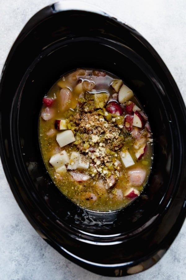 A black slow cooker insert with raw ingredients for Slow Cooker Chicken Chile Verde Stew. 