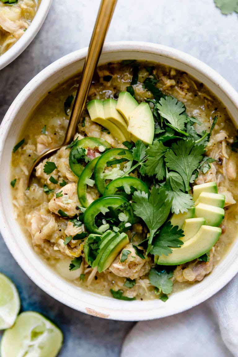 Overhead view of a bowl of slow cooker chicken Chili Verde stew topped with avocado, jalapeno, and cilantro. 