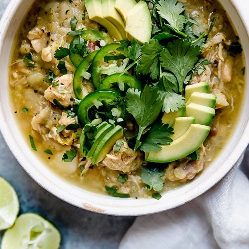 A white bowl filled with Slow Cooker Chicken Chile Verde Stew and topped with fresh cilantro, jalapeño slices, and avocado.