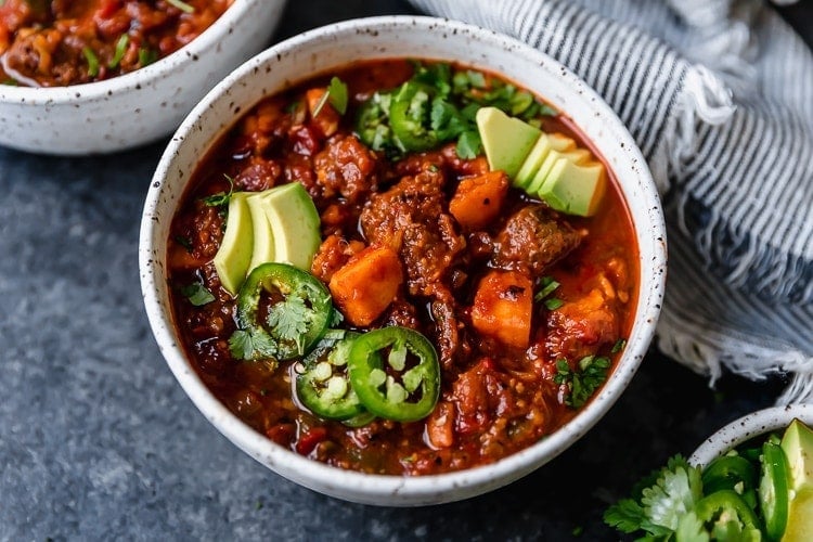 Stone bowl with serving of chunky beef chili with sweet potatoes and jalapeño slices.