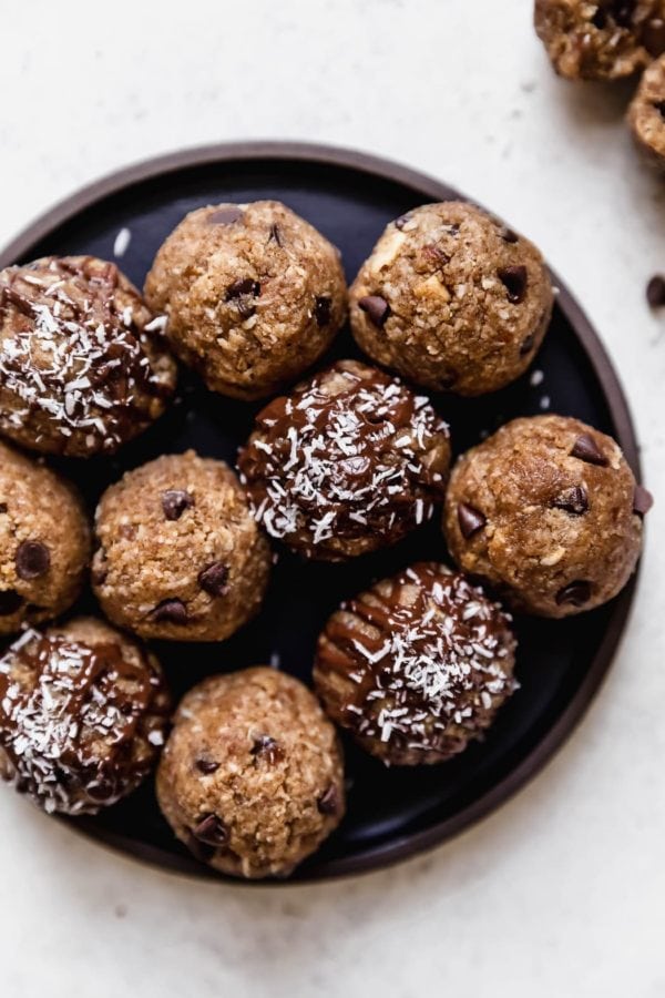 An overhead view of a black plate on a white surface that's filled with Almond Joy Protein Bites.