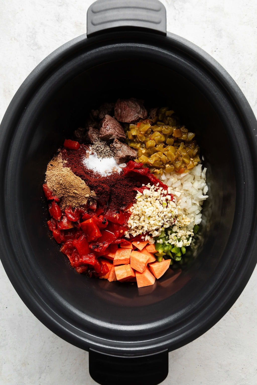 Overhead view of a slow cooker filled with ingredients for Slow Cooker Chuck Roast Chili with Sweet Potatoes ready for cooking. 