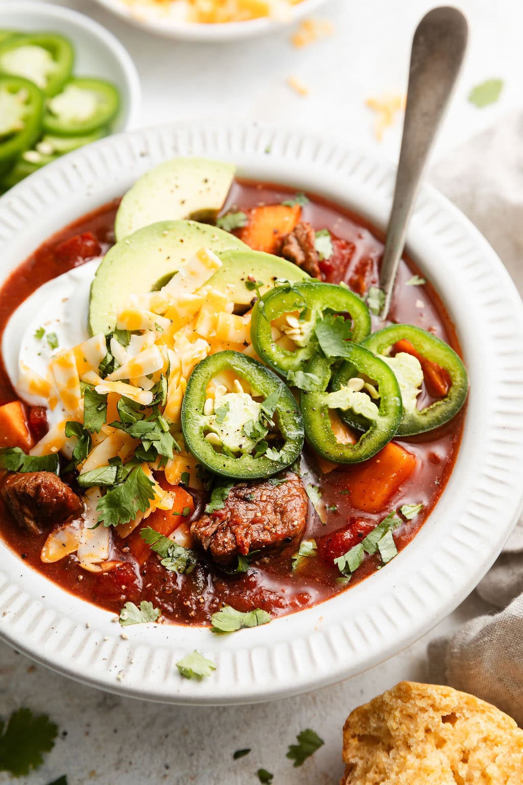 Close up view of a white bowl of Slow Cooker Chuck Roast Chili with Sweet Potatoes topped with jalapeno slices and sprinkled with cheese. 