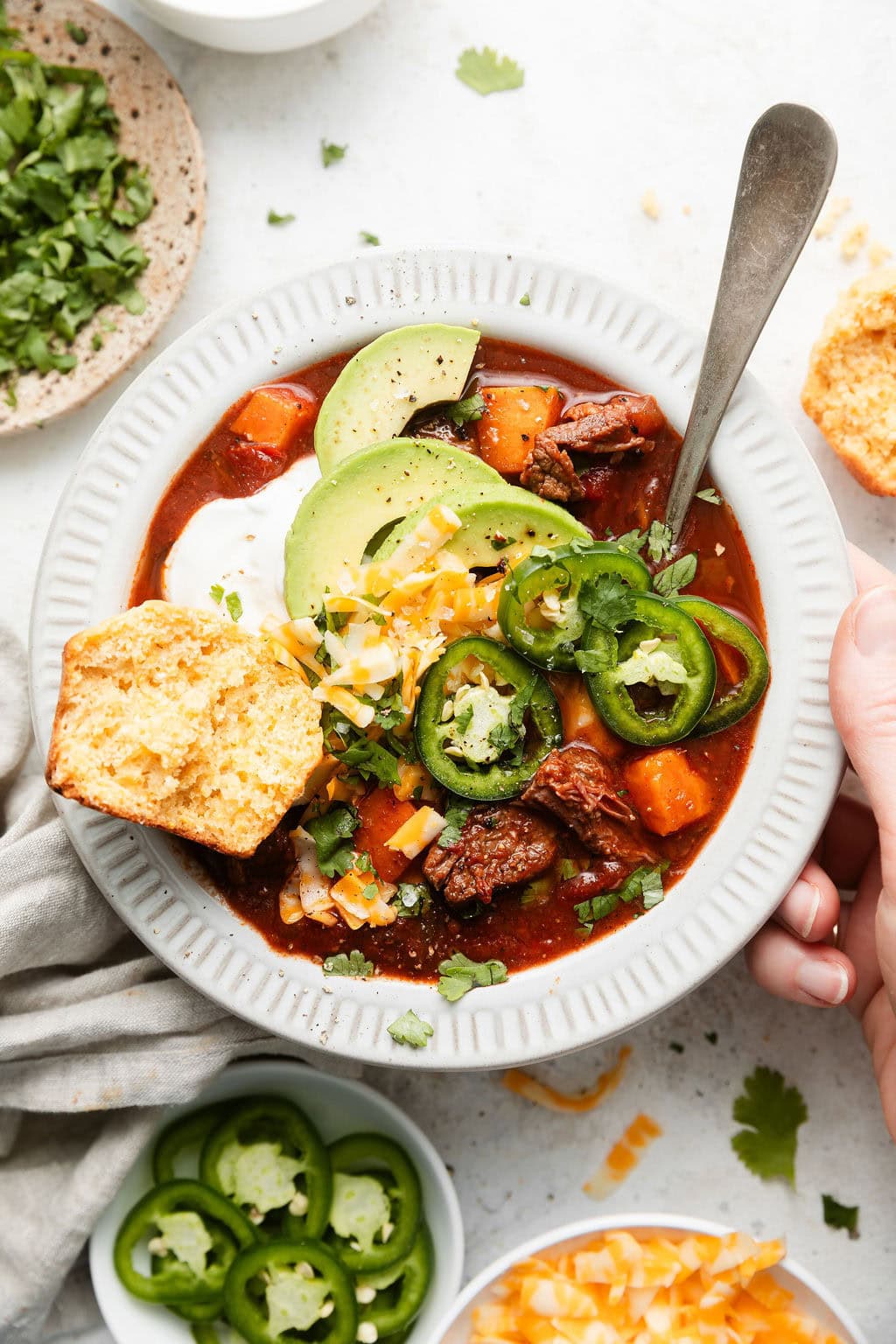Overhead view of a bowl of Slow Cooker Chuck Roast Chili With Sweet Potatoes and a corn bread muffin on the side. 