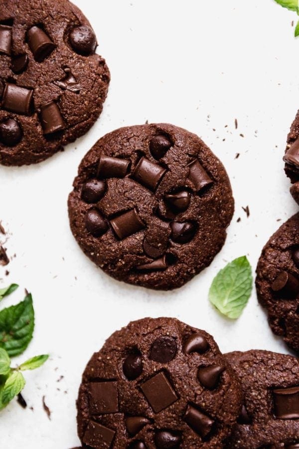 Overhead view of Low Sugar Double Chocolate Mint Cookies on a white surface that are studded with chocolate chips and chunks. 