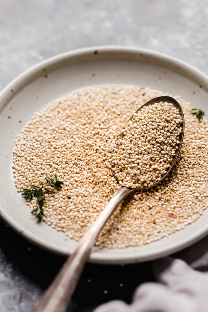 Shallow bowl filled with uncooked quinoa, a spoon in quinoa 