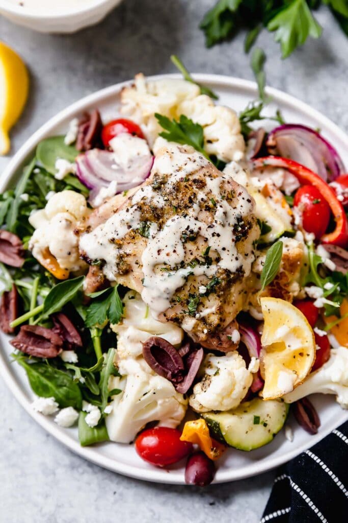 Overhead view serving of mediterranean chicken served over vegetables with sauce on top