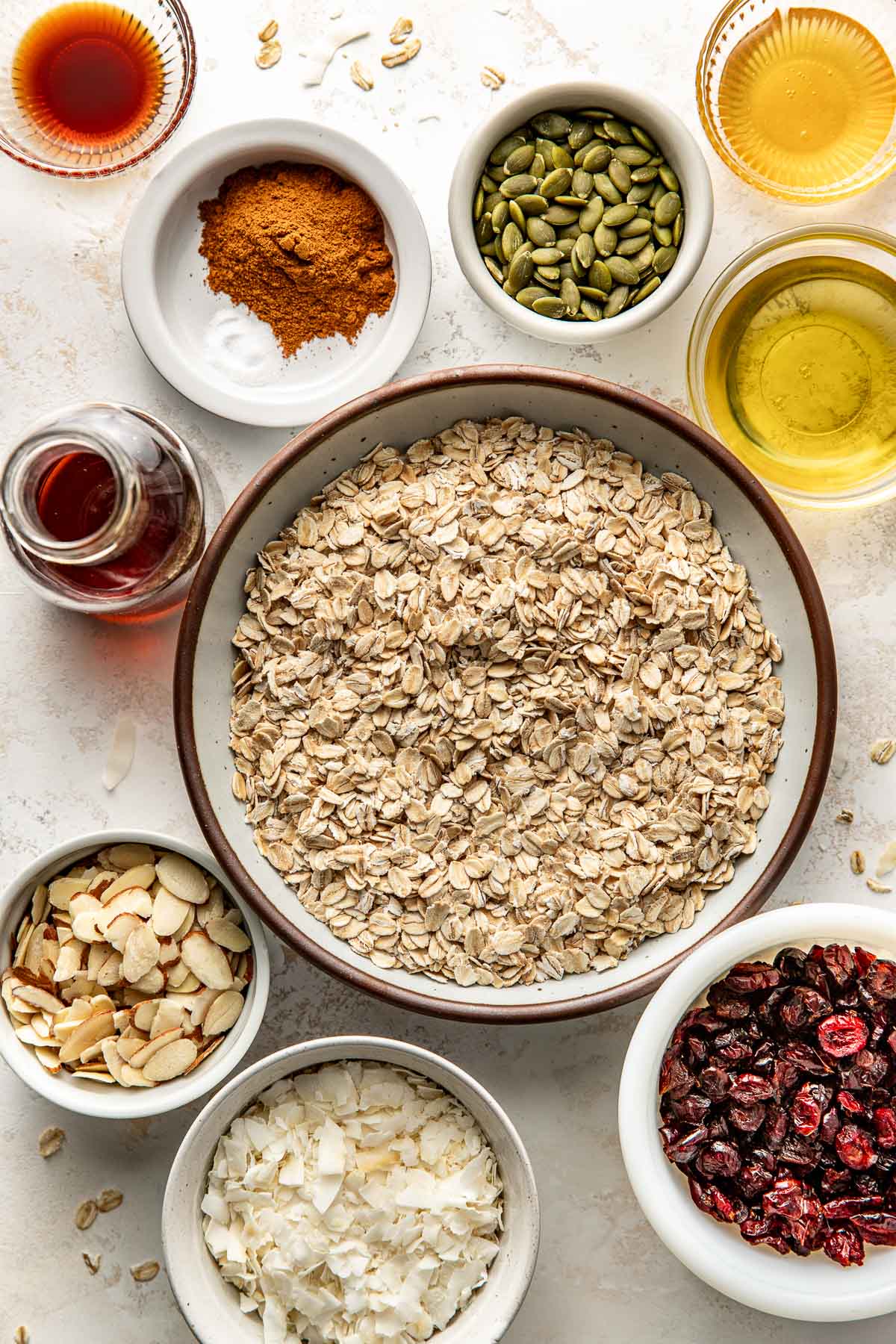 Overhead view of a variety of ingredients for Homemade Granola in different sized bowls. 