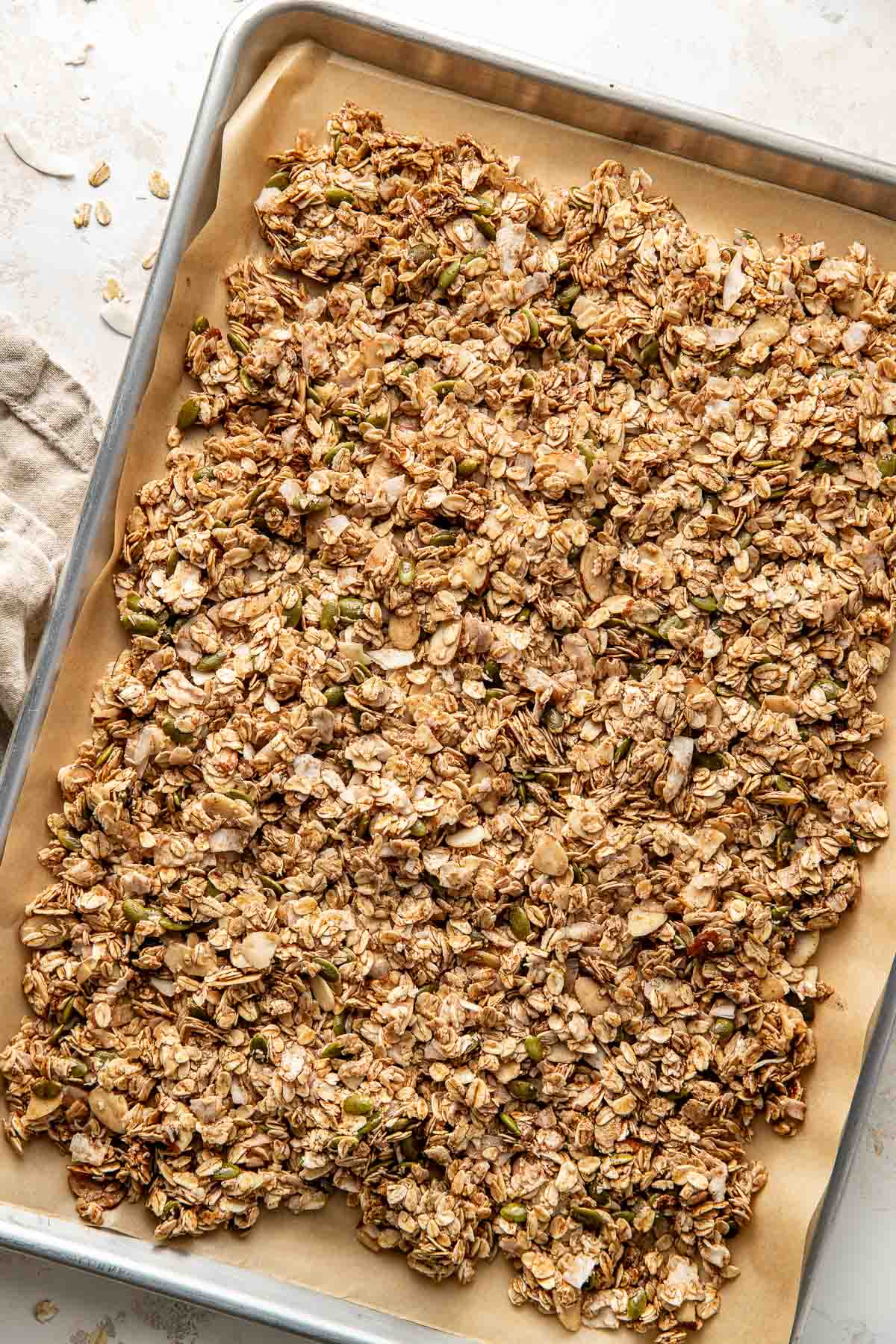 Overhead view of a parchment lined sheet pan filled with a granola mixture evenly spread throughout the surface of the pan. 