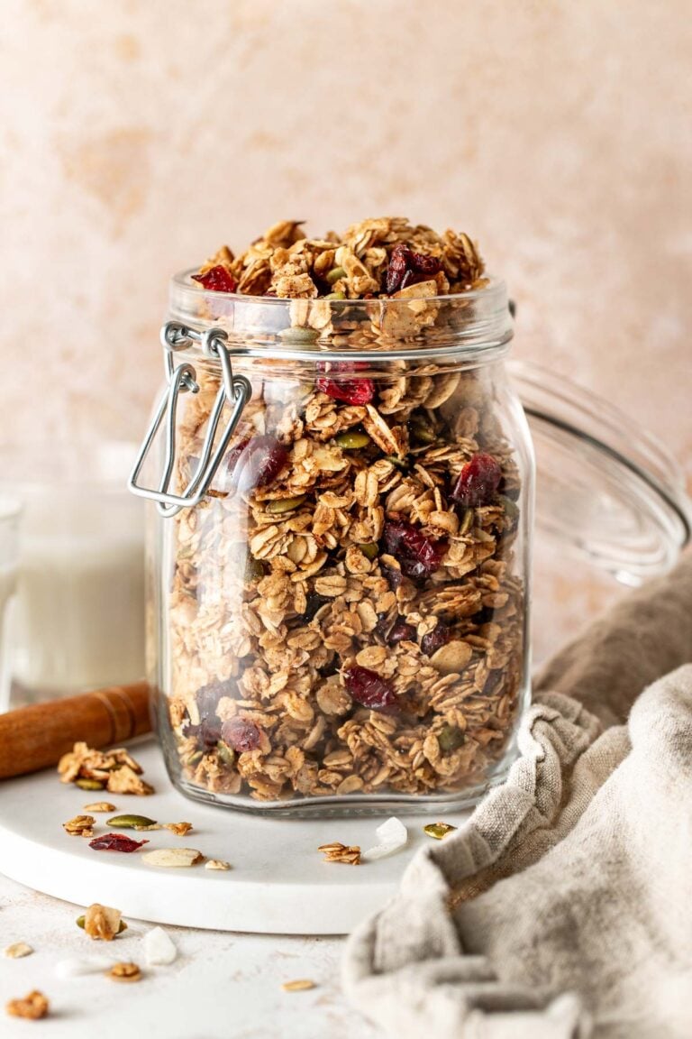 Close up view of a glass jar filled with homemade granola on a marble countertop.