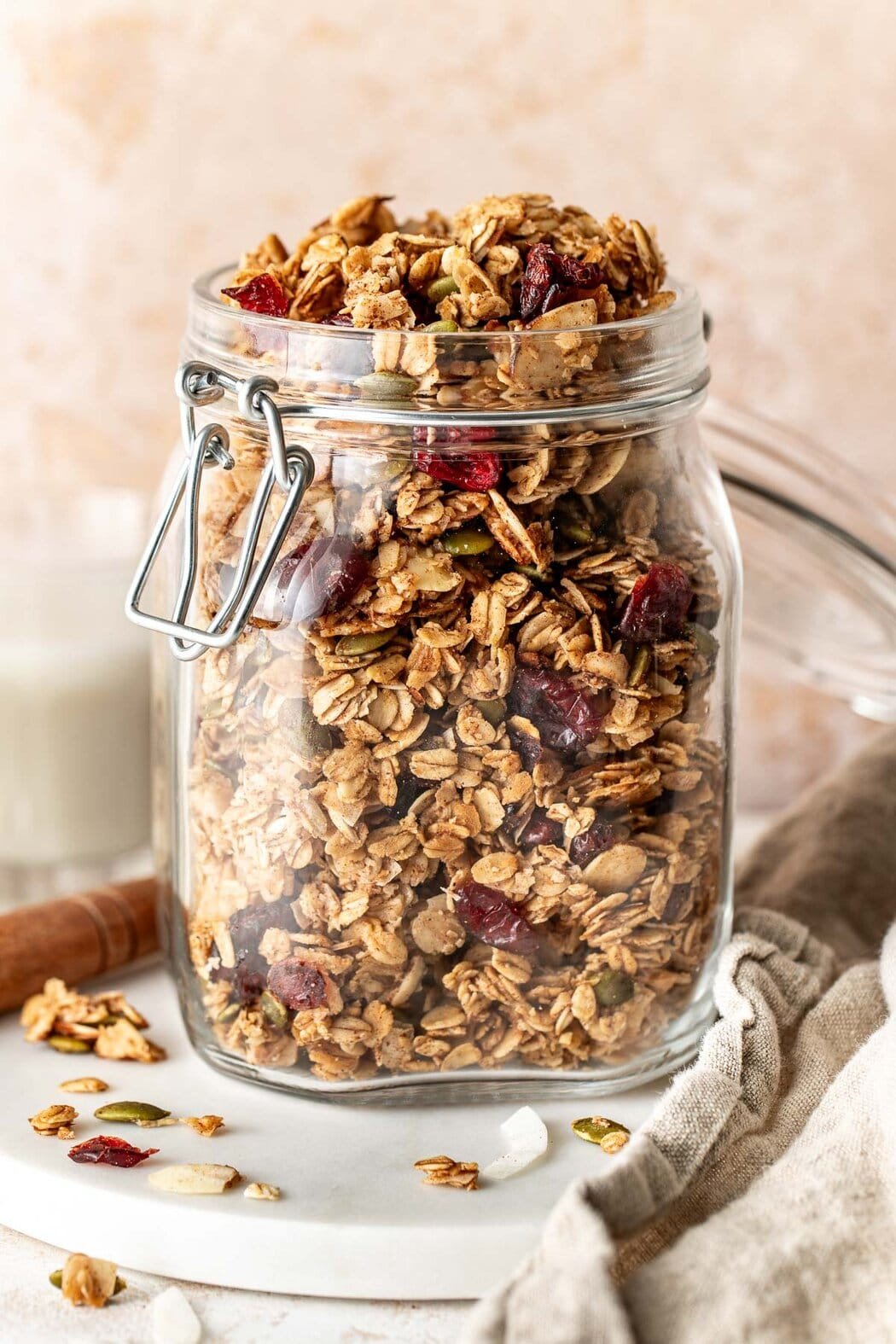 Side view of a glass jar filled with homemade granola showing the crunchy texture and pieces of dried fruit and pumpkin seeds throughout the mixture. 