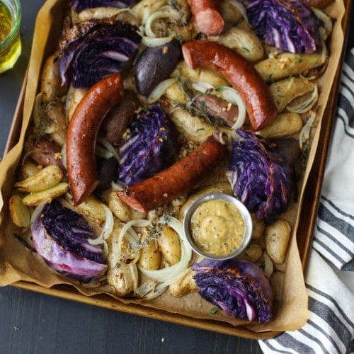 Overhead view of Sheet Pan Kielbasa Cabbage and Potatoes on a dark background with a white towel and a glass of lager off to the side.