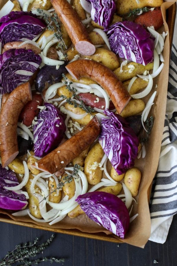 Overhead shot of a potatoes, onions, purple cabbage, and kielbasa on a parchment-lined pan to make Sheet Pan Kielbasa, Cabbage and Potatoes.