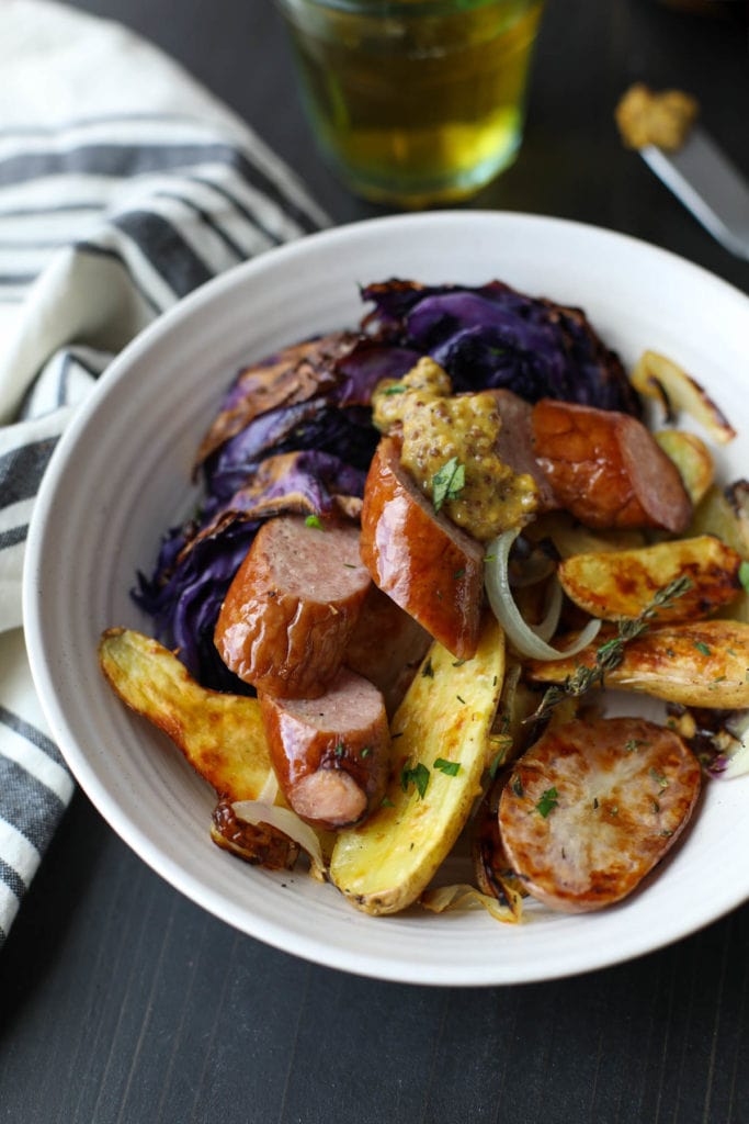 A bowl filled with sheet pan kielbasa, cabbage, and potatoes topped with stone ground mustard 